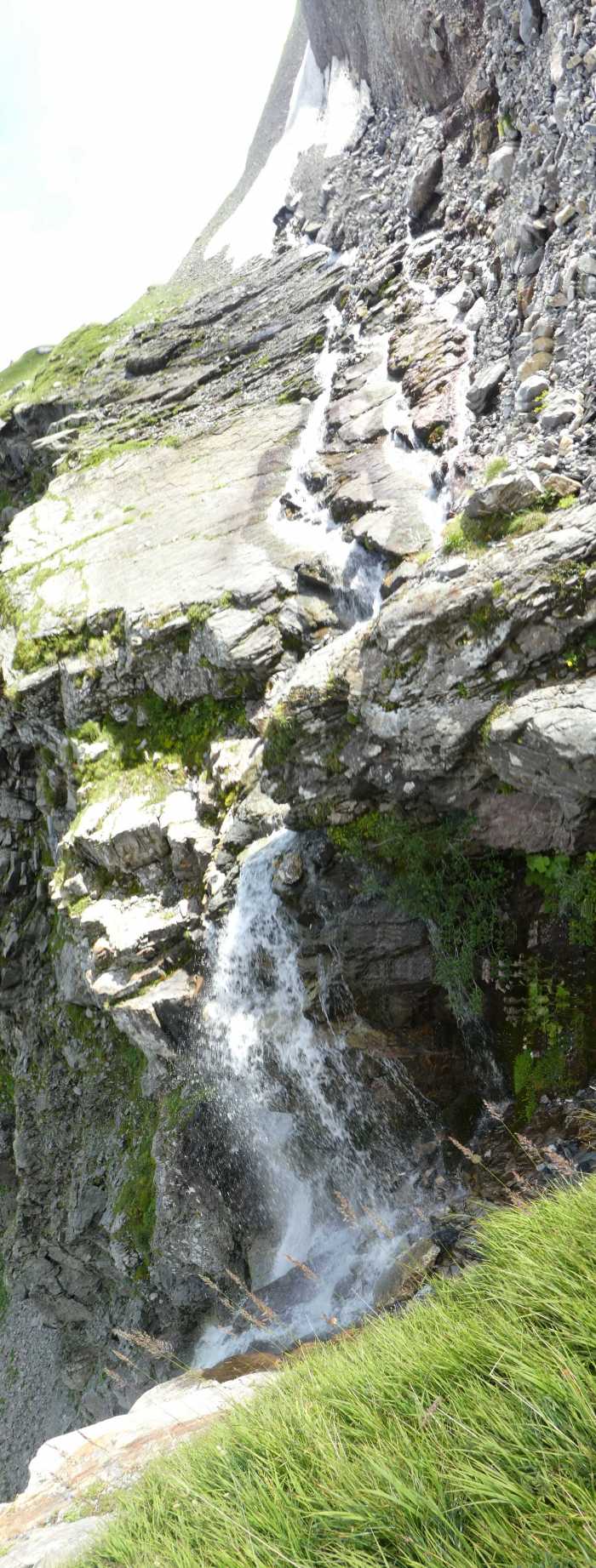 Cascade dangereuse psychédélique, prise en mode panorama diagonal le pente paraît beaucoup plus raide que la réalité (on peut s'en faire un idée en rétablissant la verticalité de la chute d'eau et des brins d'herbes), le danger ne réside pas tant dans la pente du chemin, mais plutôt en cas de course de vitesse à la descente avec petite distraction (le chemin fait un angle droit mal marqué et 4 mètres plus loin on est dans la cascade).